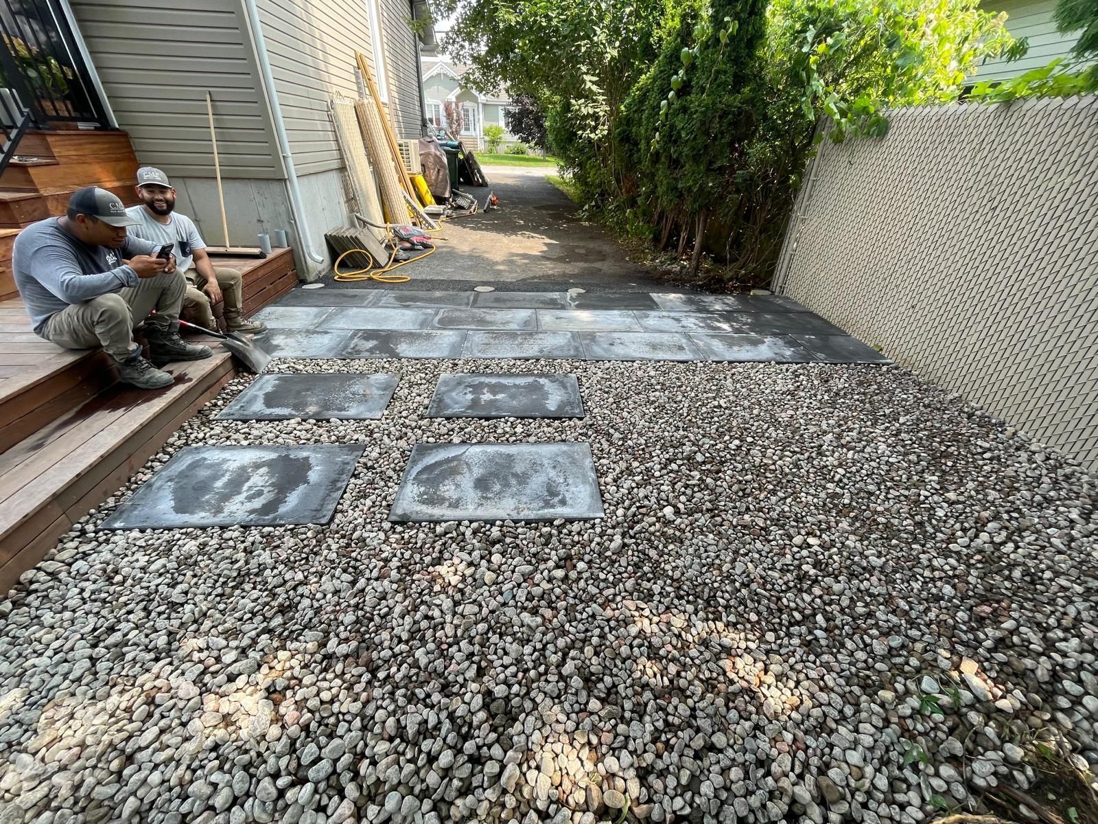 Deux hommes sont assis sur les marches d'une maison dans une cour de gravier.