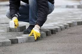 Un homme portant des gants jaunes pose des briques sur un trottoir.