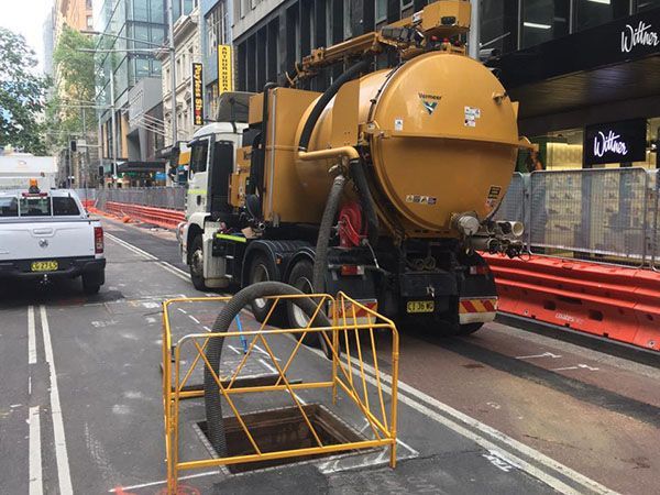 A yellow vacuum truck is driving down a city street.
