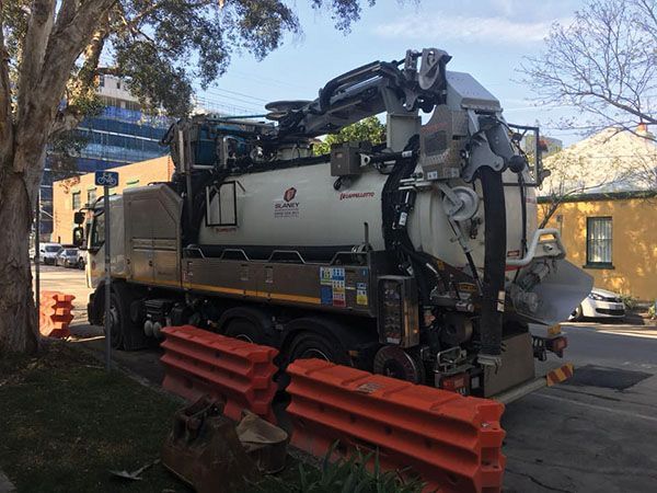 A vacuum truck is parked on the side of the road next to a tree.