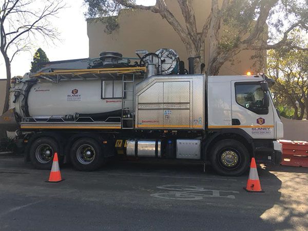 A vacuum truck is parked in a parking lot next to two orange cones.