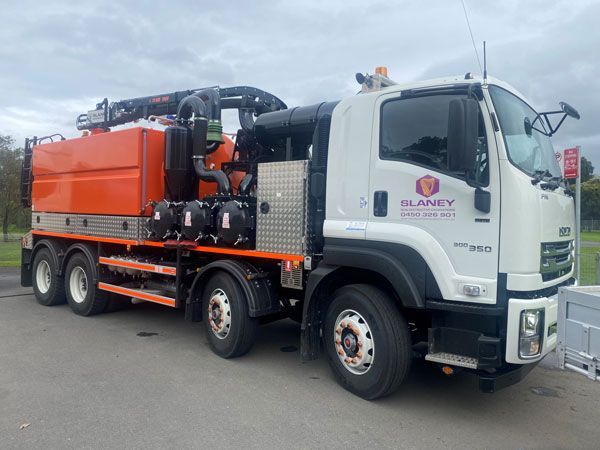 A white and orange vacuum truck is parked on the side of the road.