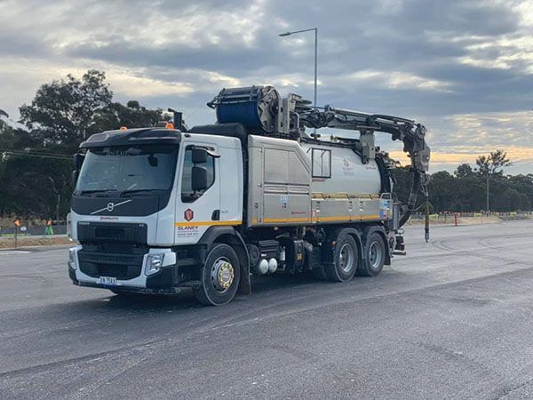 A vacuum truck is driving down a street in a parking lot.