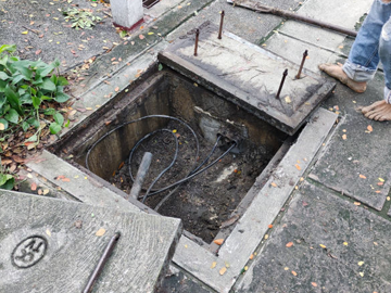 A man is standing in a hole in the ground next to a manhole cover.