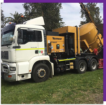 A yellow vermeer truck is parked next to a white truck.