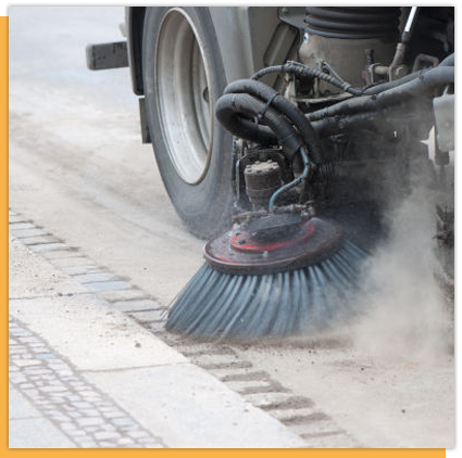 A truck is sweeping the sidewalk with a brush