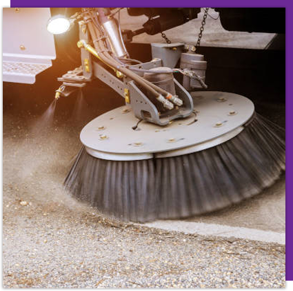 A street sweeper is cleaning the ground with a large brush.