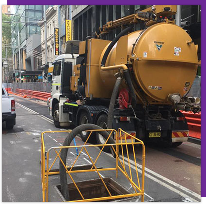 A yellow vacuum truck is driving down a city street.