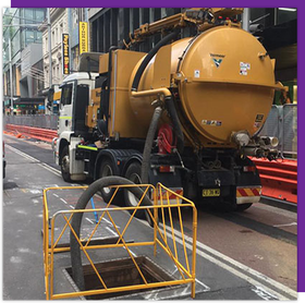 A yellow vacuum truck is driving down a city street.