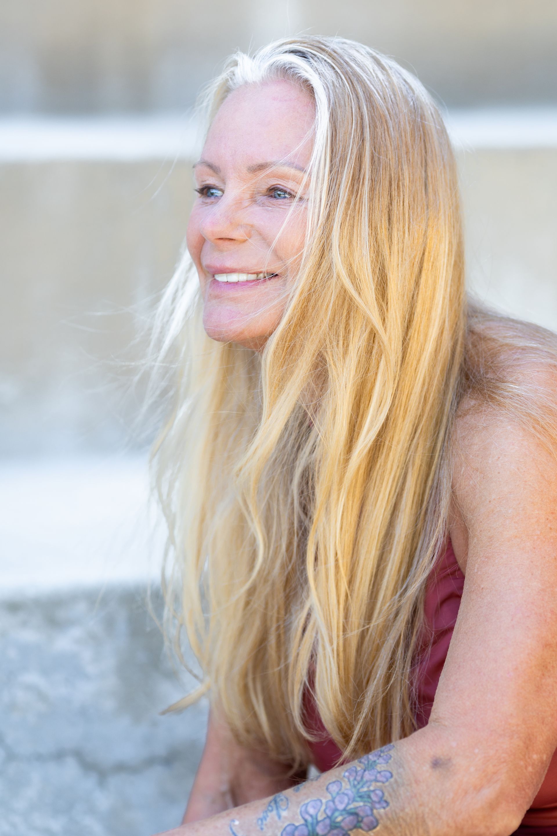A woman with long blonde hair and a tattoo on her arm is smiling.