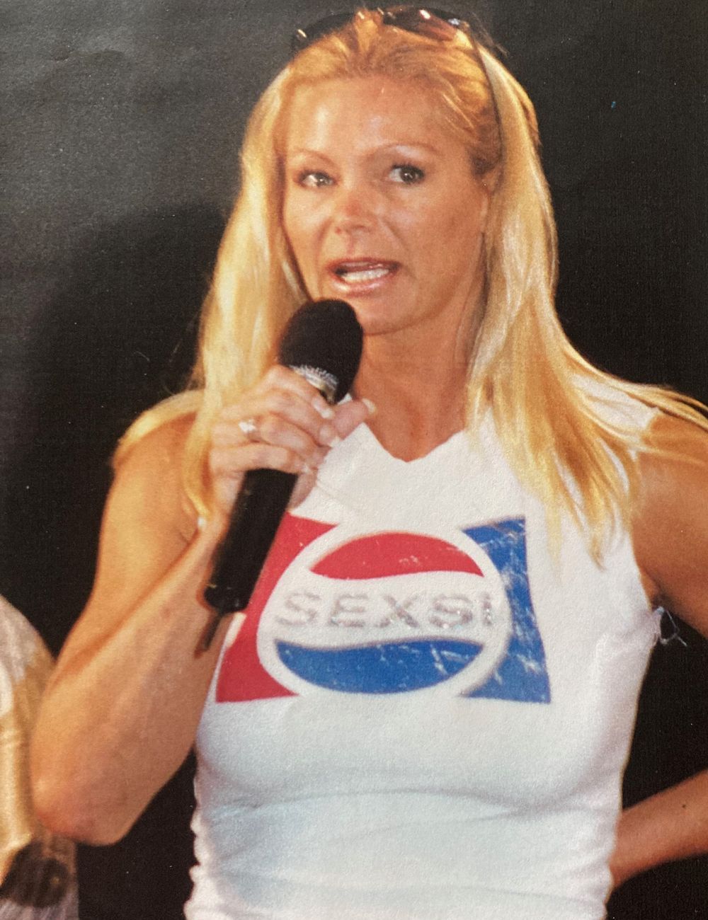 A woman wearing a pepsi shirt is speaking into a microphone