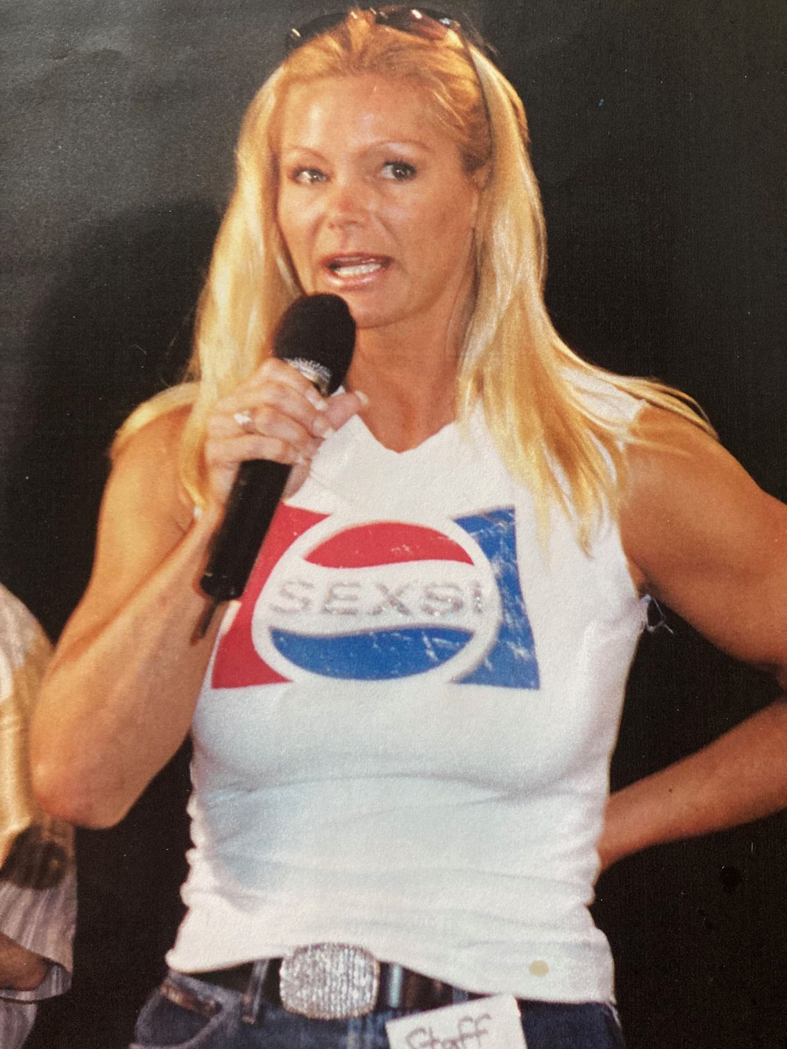 A woman wearing a pepsi shirt is speaking into a microphone