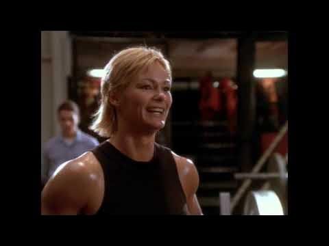 A woman in a black tank top is smiling in a gym.