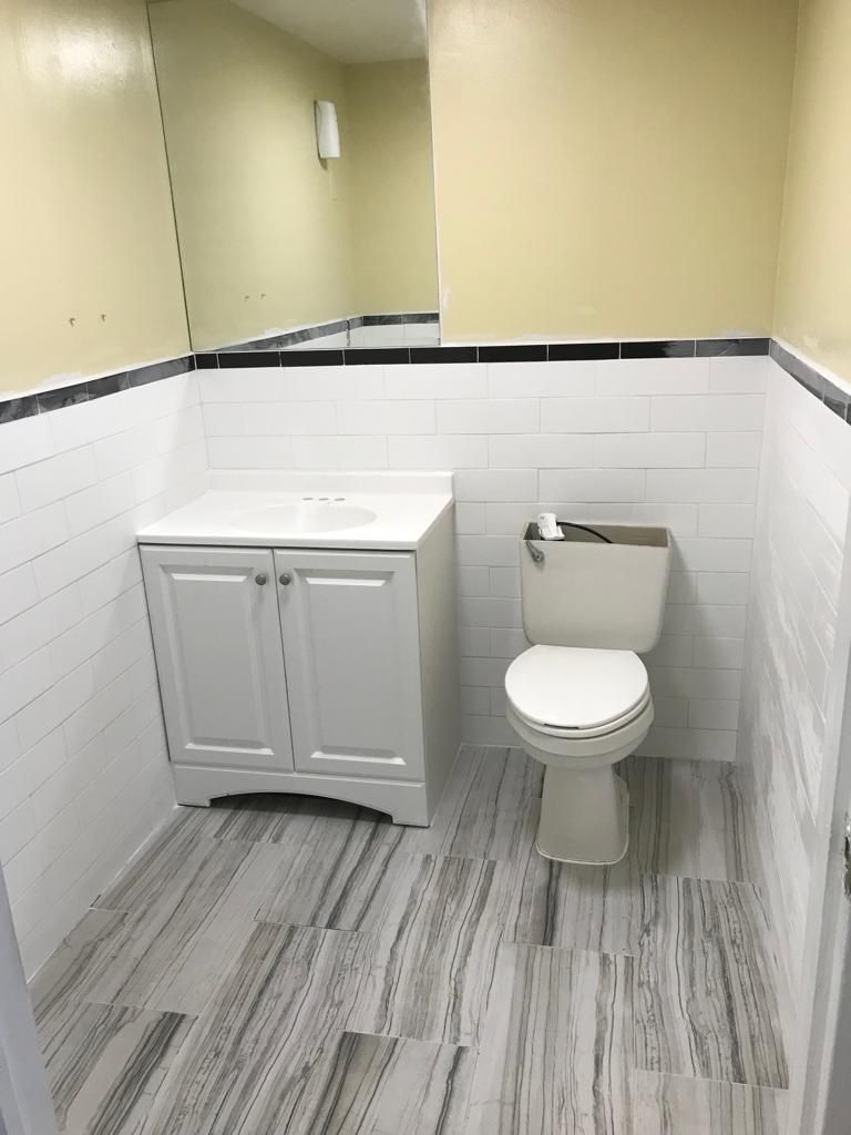 Bathroom with white tile walls, a white vanity, and a toilet; gray and white floor.