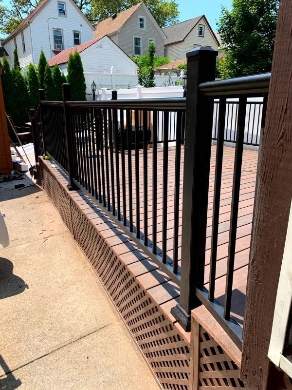 Black deck railing with vertical bars; brown lattice and decking. Houses in the background.