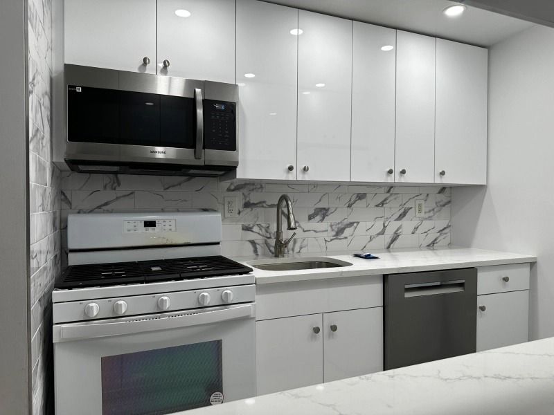 White kitchen with stainless steel appliances, marble backsplash, and white cabinets.