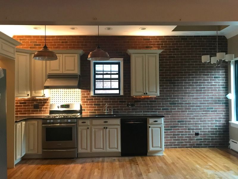 Kitchen with brick wall, cream cabinets, stainless steel appliances, and wooden floors.