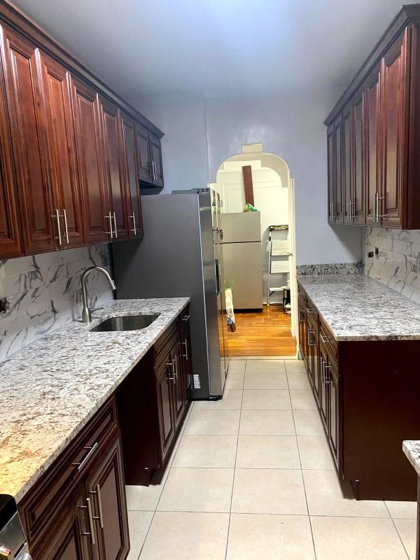 Dark wood kitchen with granite countertops, stainless steel appliances, and a doorway to another room.