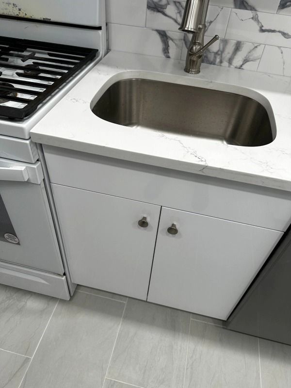 White kitchen cabinets with a stainless steel sink, next to a stove.