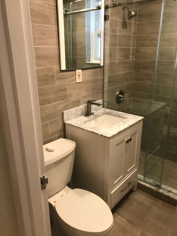Small bathroom with a white vanity, toilet, and shower with glass doors. Beige tile walls.