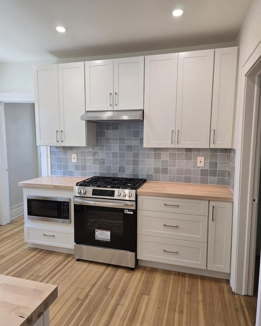 Kitchen with white cabinets, wooden counters, stainless steel appliances, and a gray tile backsplash.