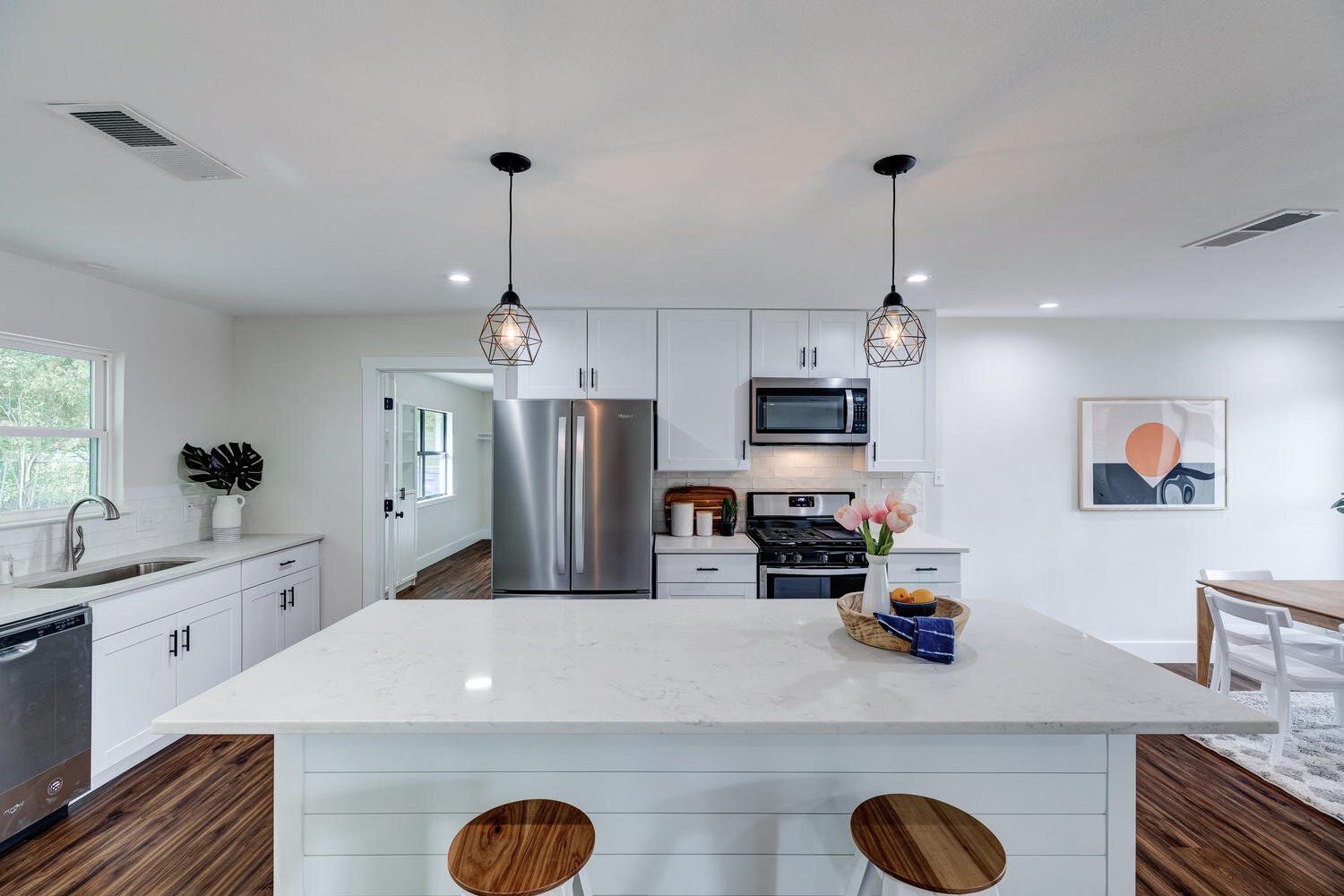 Modern white kitchen with an island, stainless steel appliances, and two pendant lights.