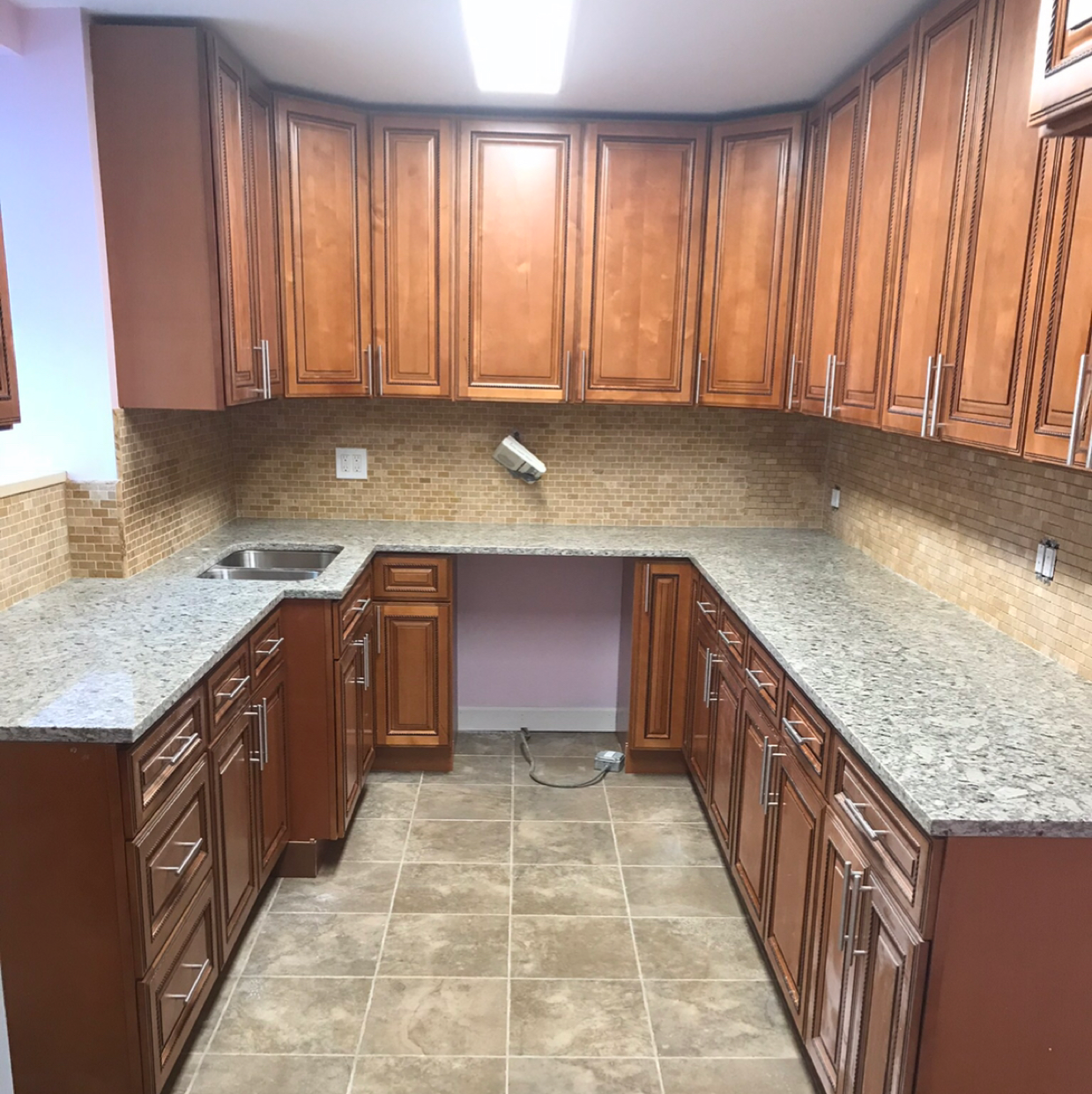 White kitchen seen through a pass-through, with white counters, cabinets, appliances, and marbled backsplash.