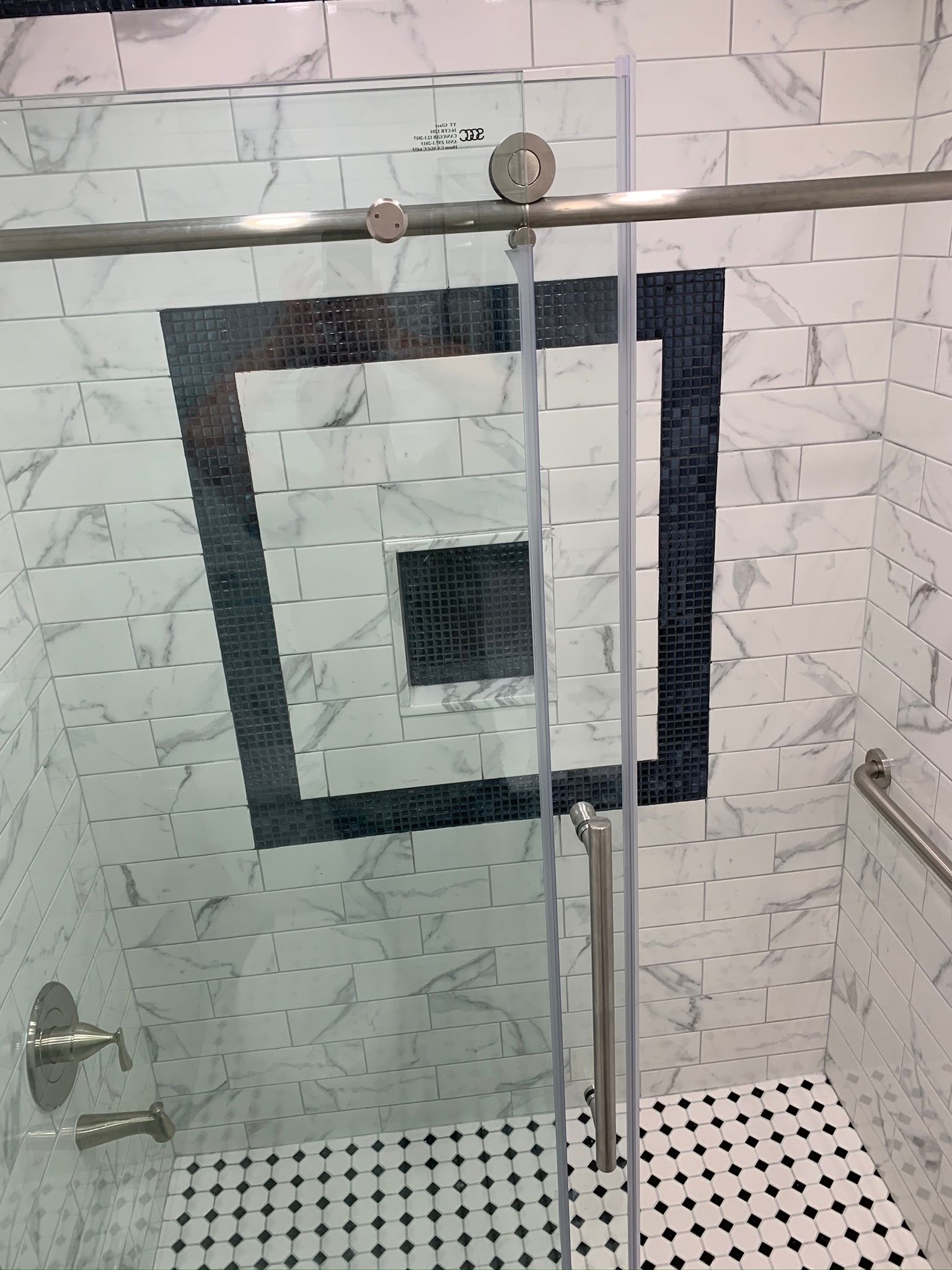 Shower with sliding glass door, marble and black tile design. Stainless steel fixtures, handrail.