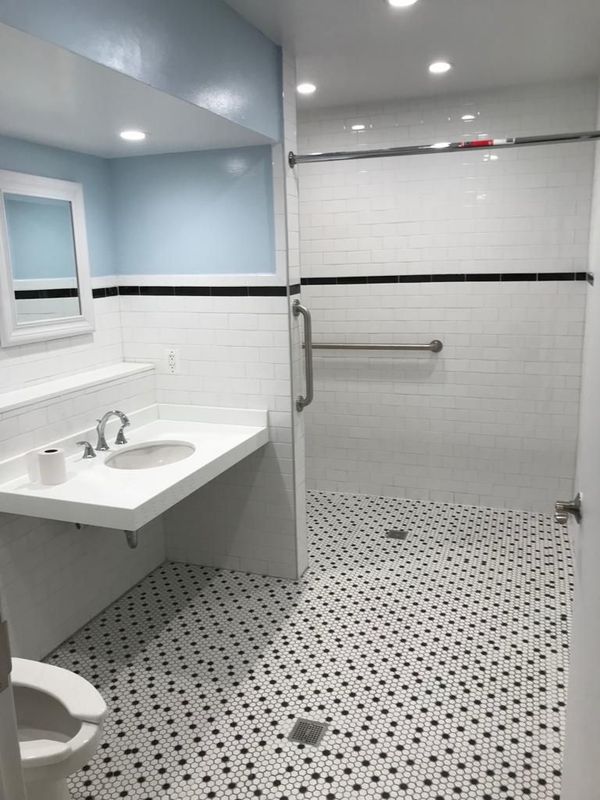 Accessible bathroom with a glass shower, white tiles, and black and white patterned floor.