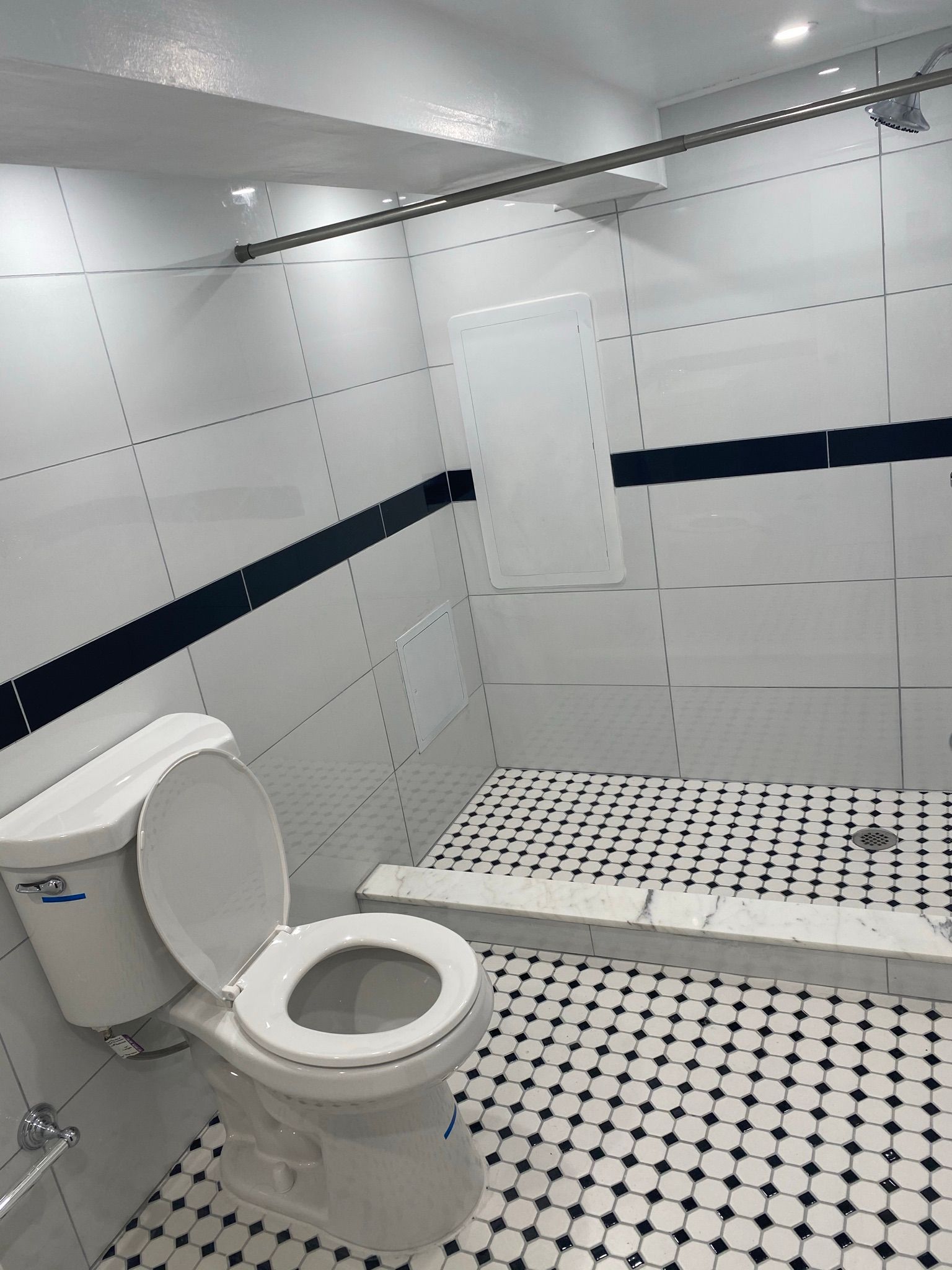 A white tiled bathroom with a toilet, black and white floor, and a shower area.