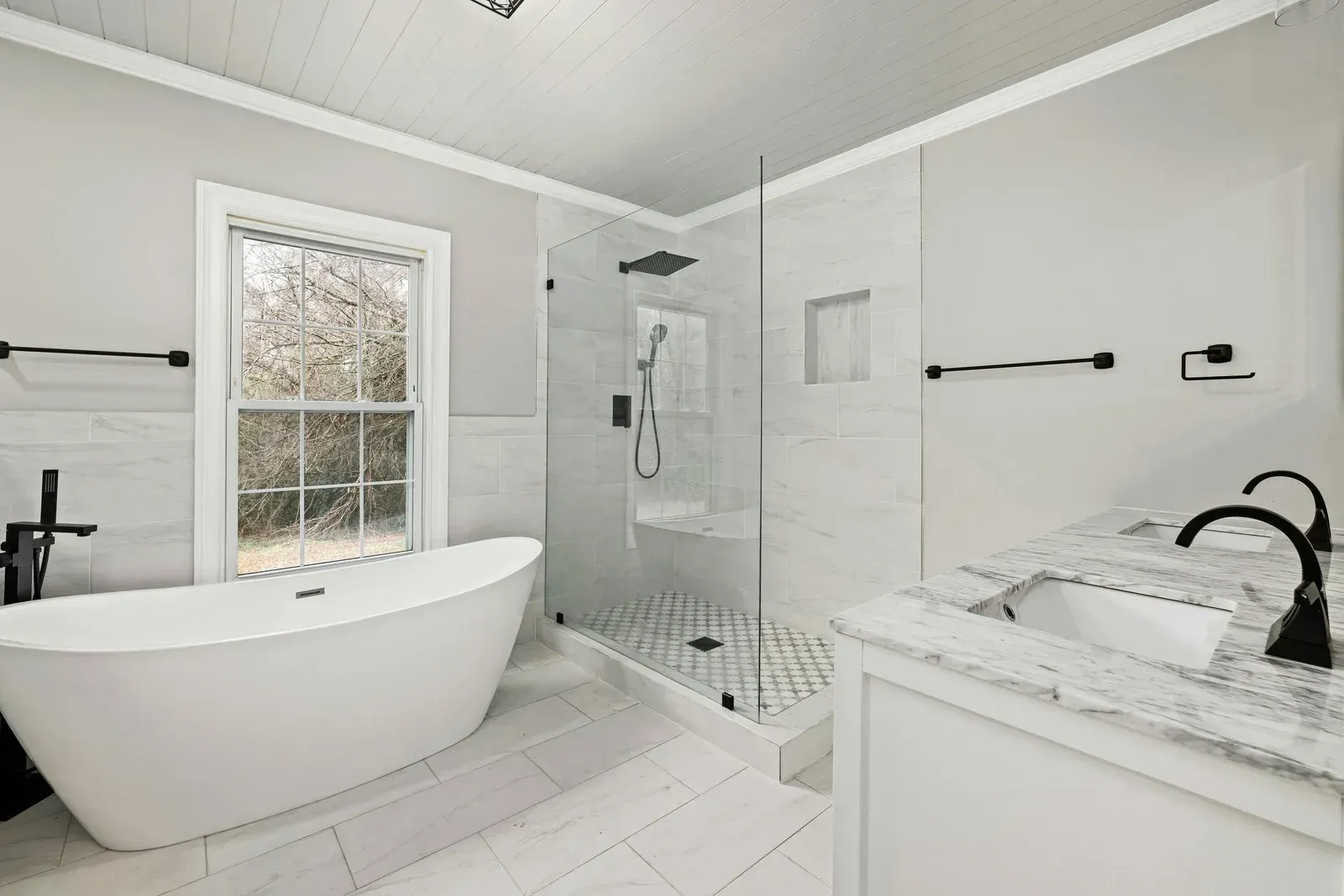 Bathroom with white tub, shower, vanity, marble countertops, and black fixtures.
