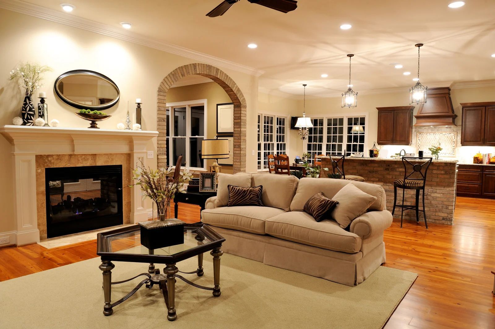 Living room with fireplace, archway to kitchen, sofa, coffee table, hardwood floors, and overhead lighting.