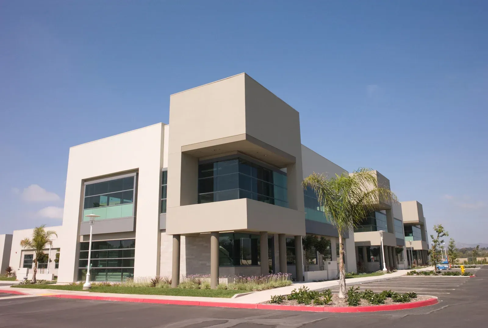 Modern, two-story office building with beige and gray facade, large windows, and a bright blue sky.