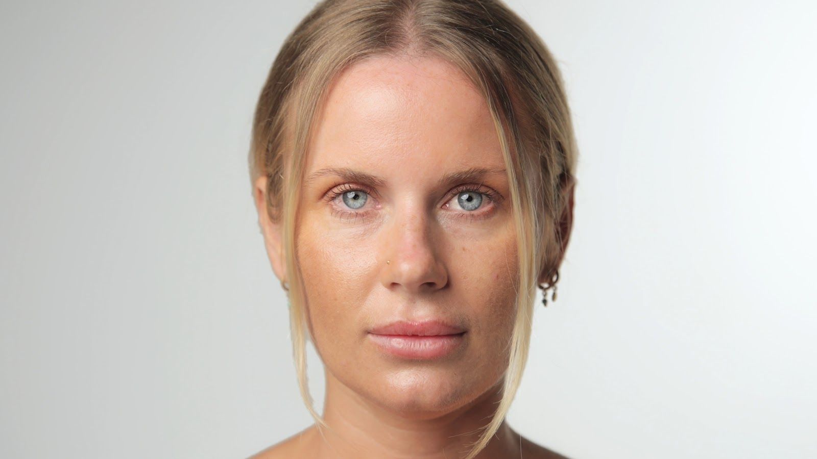 Woman with blonde hair, pale skin, and blue eyes looking at the viewer against a white background.