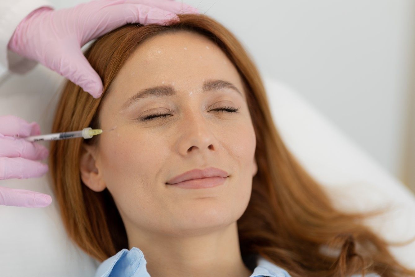 Person receiving a facial injection near the eye, with a gloved hand holding a syringe.