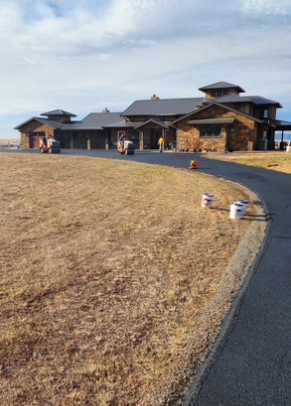 A newly paved black asphalt driveway between two houses with a bright orange traffic cone in the foreground.