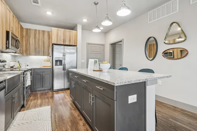 Modern kitchen with a gray island, wooden cabinets, stainless steel appliances, and decorative wall mirrors.