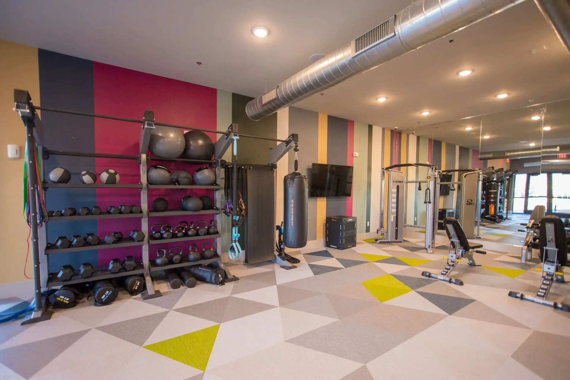 A modern gym with a weight rack, punching bag, and exercise machines on a geometric patterned floor.