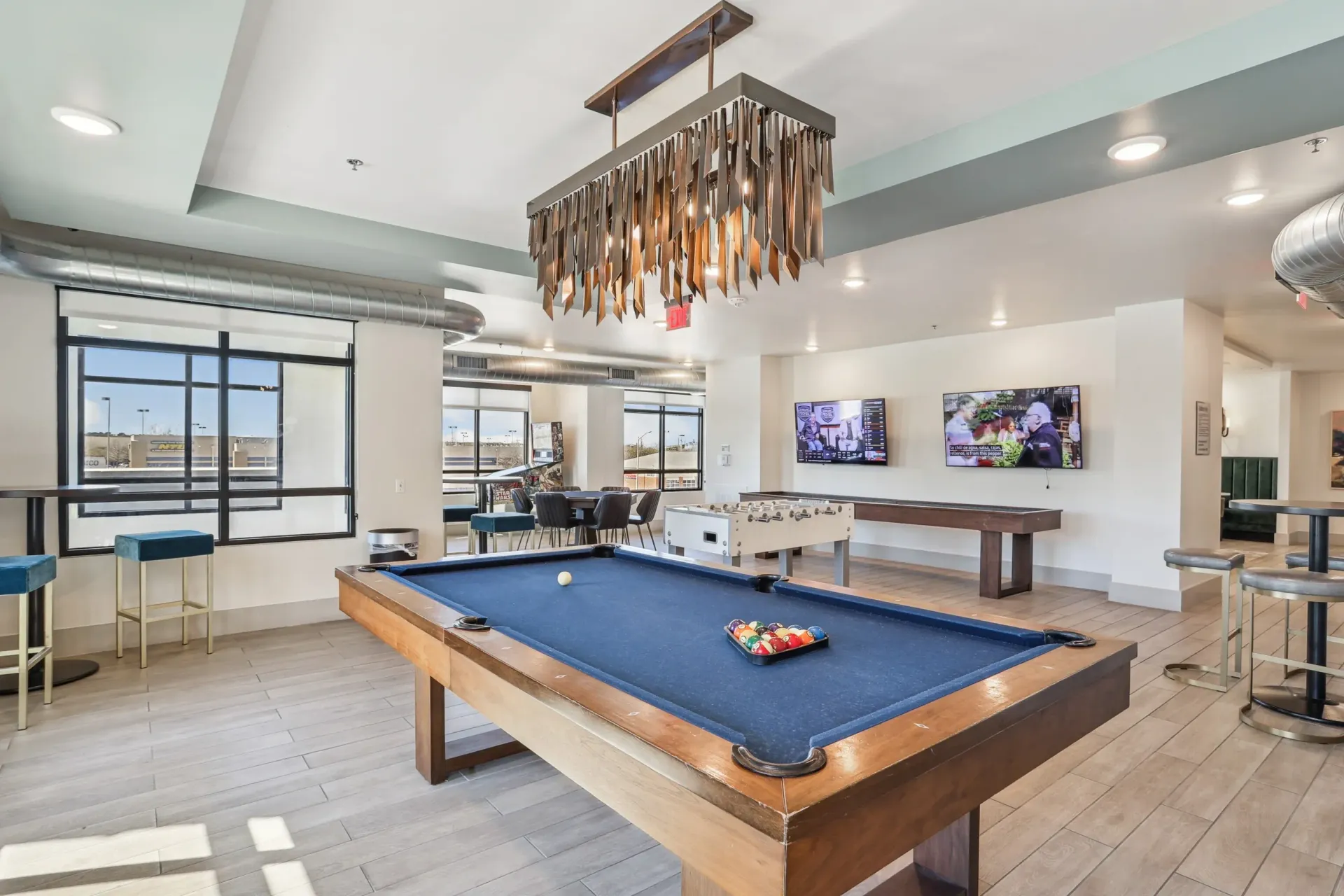 A game room with a blue pool table, a foosball table, high-top seating, and a decorative chandelier.