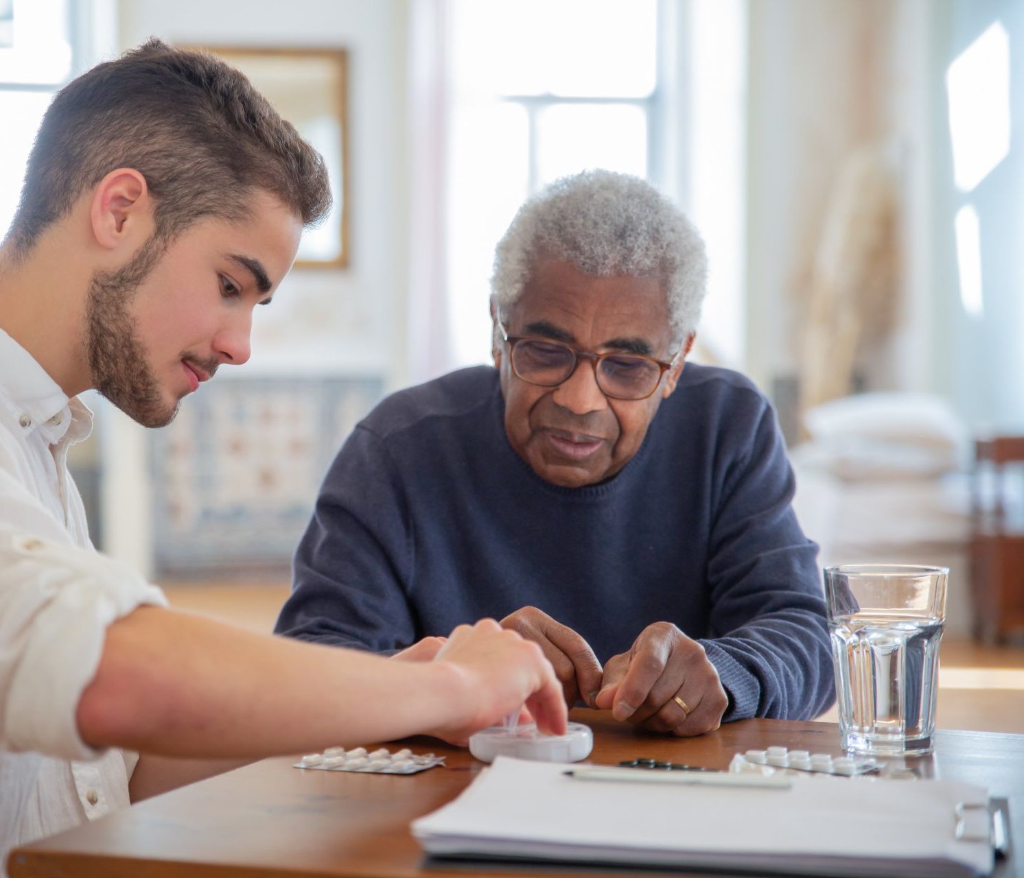 A young man is helping an older man with his medication.
