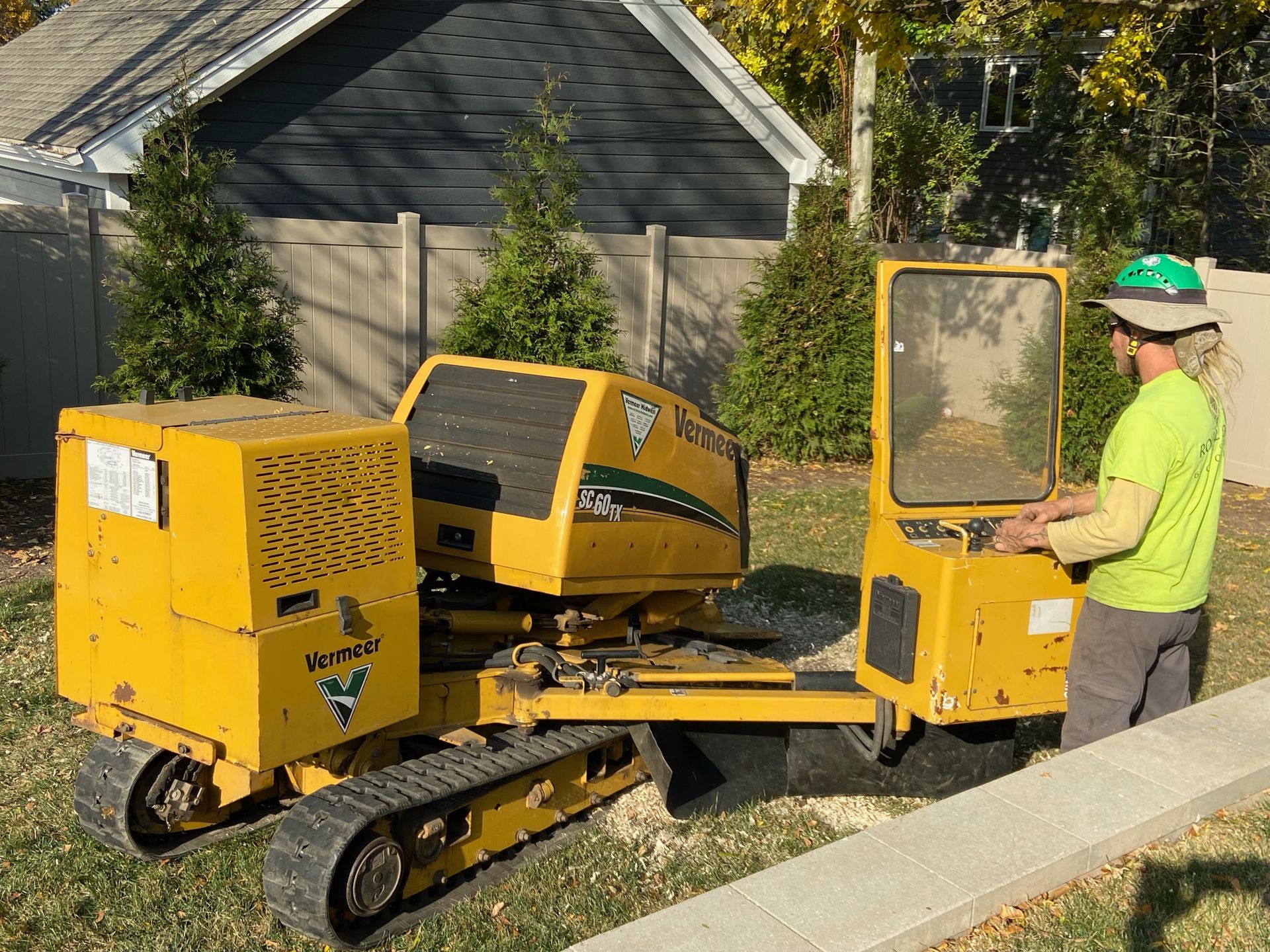 Man operating a yellow stump grinder in a yard.
