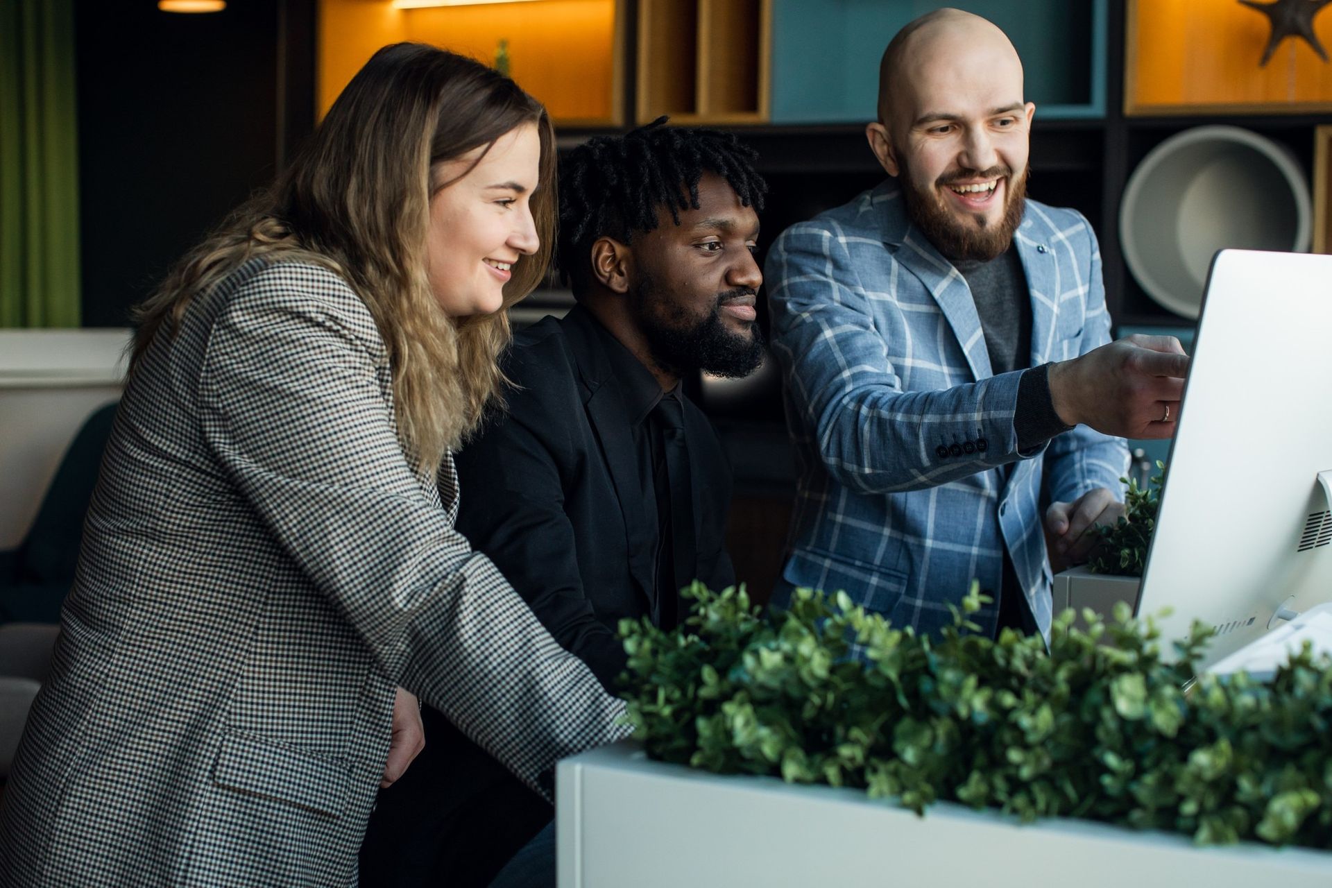 Three people looking at a computer screen, discussing something. One points. Greenery in the foreground.