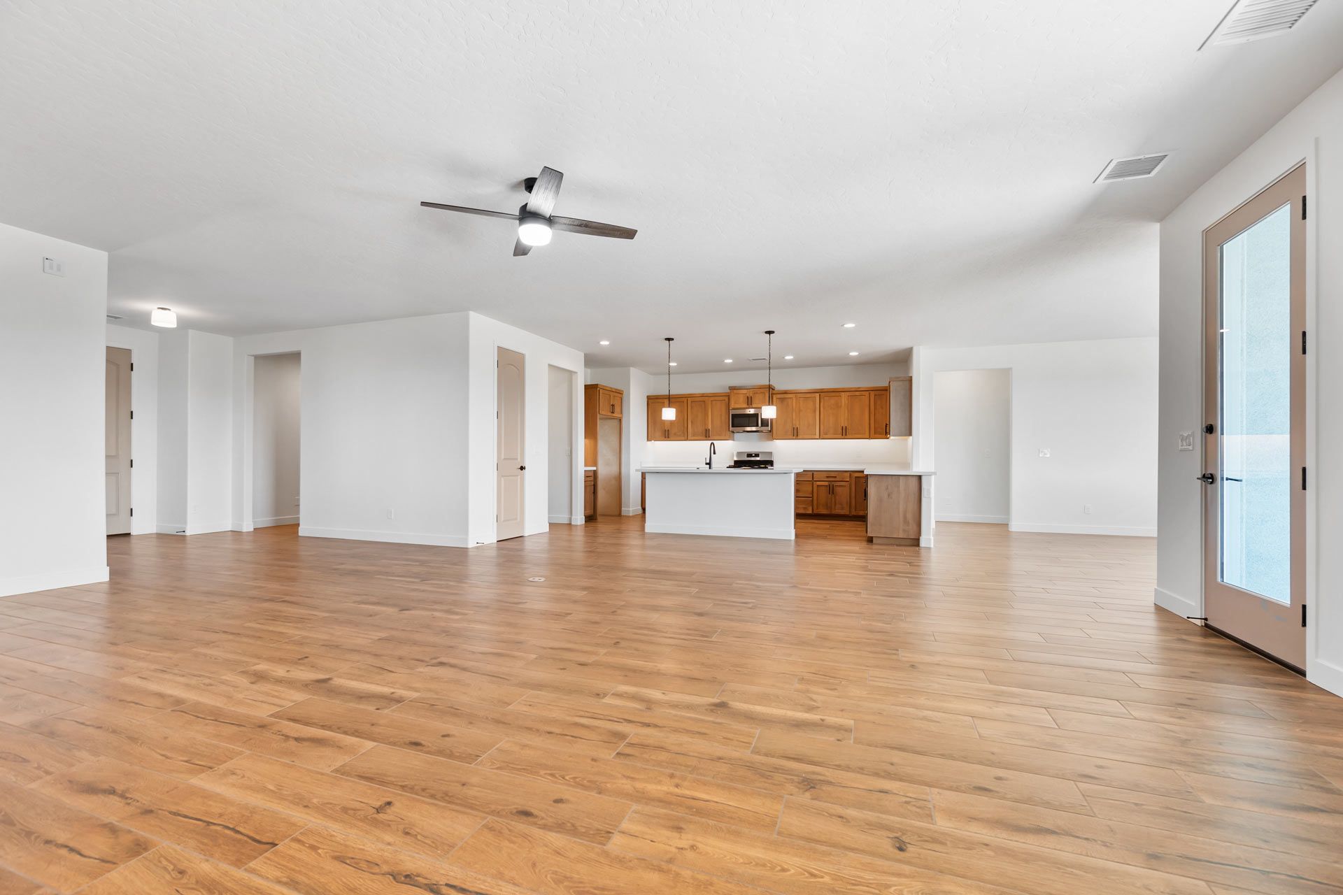 Open-concept living space with hardwood floors, white walls, and a kitchen in the background.