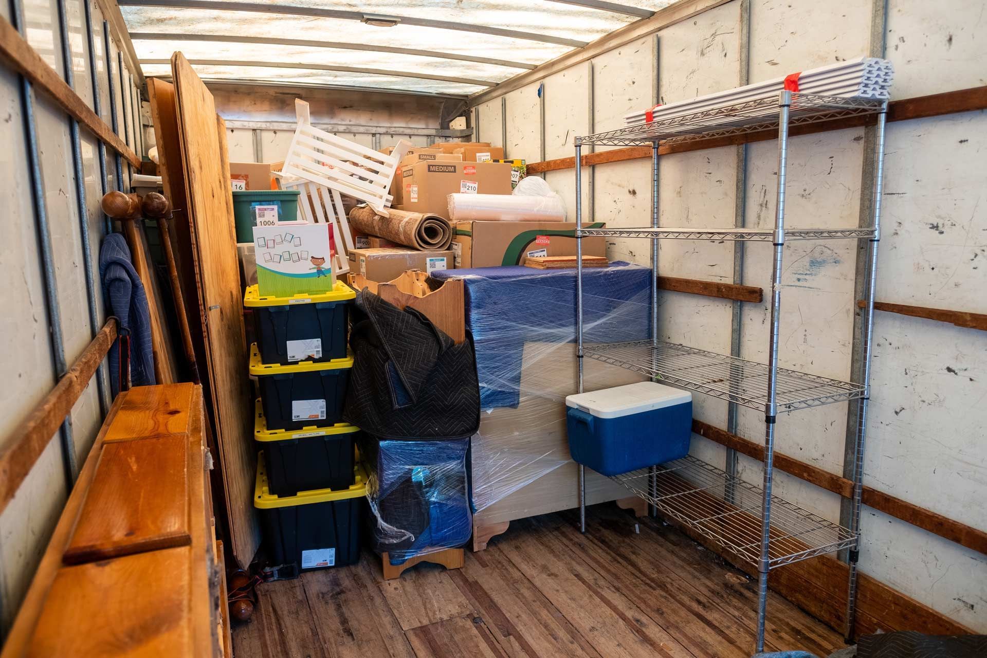 Interior of a moving truck packed with boxes, furniture, bins, and a metal shelving unit.