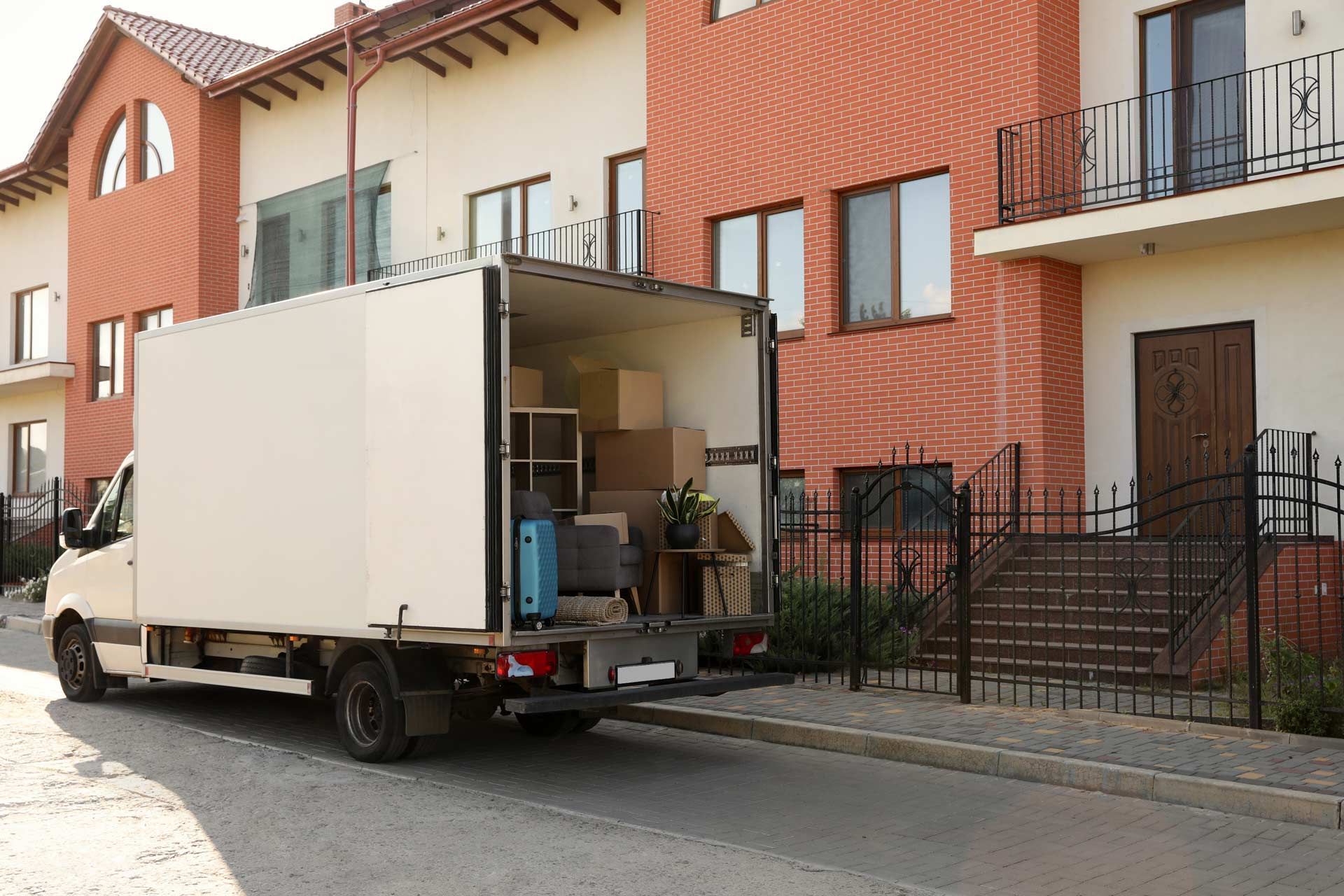 Moving truck parked in front of a brick building, loading or unloading boxes and furniture.