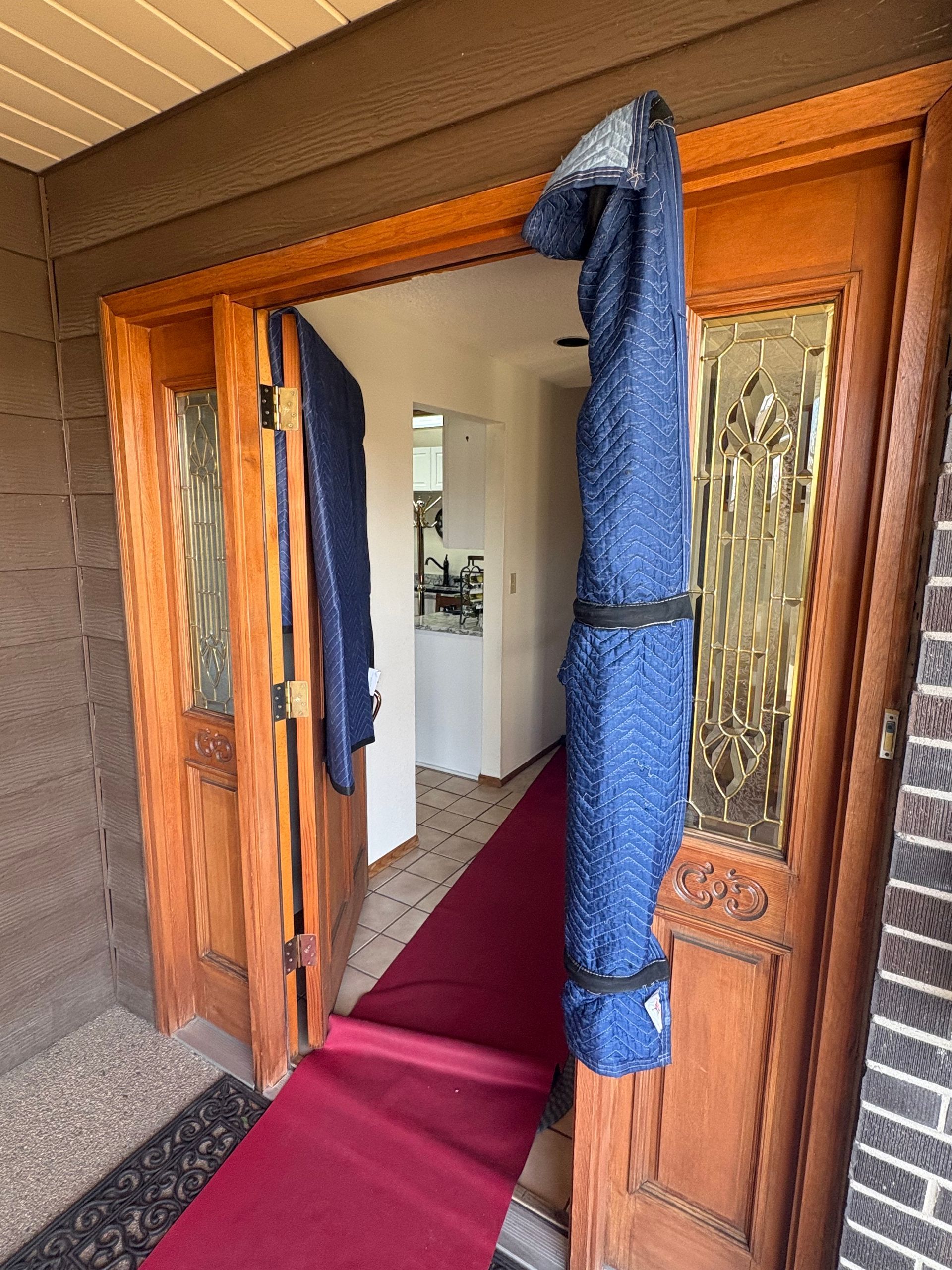 Open wooden front doors with a red carpet leading inside; a blue roll is hanging on a door.
