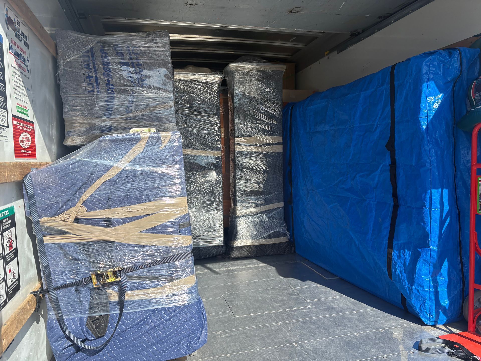 Inside a moving truck packed with wrapped furniture. Items covered in blue, silver, and clear wrap.