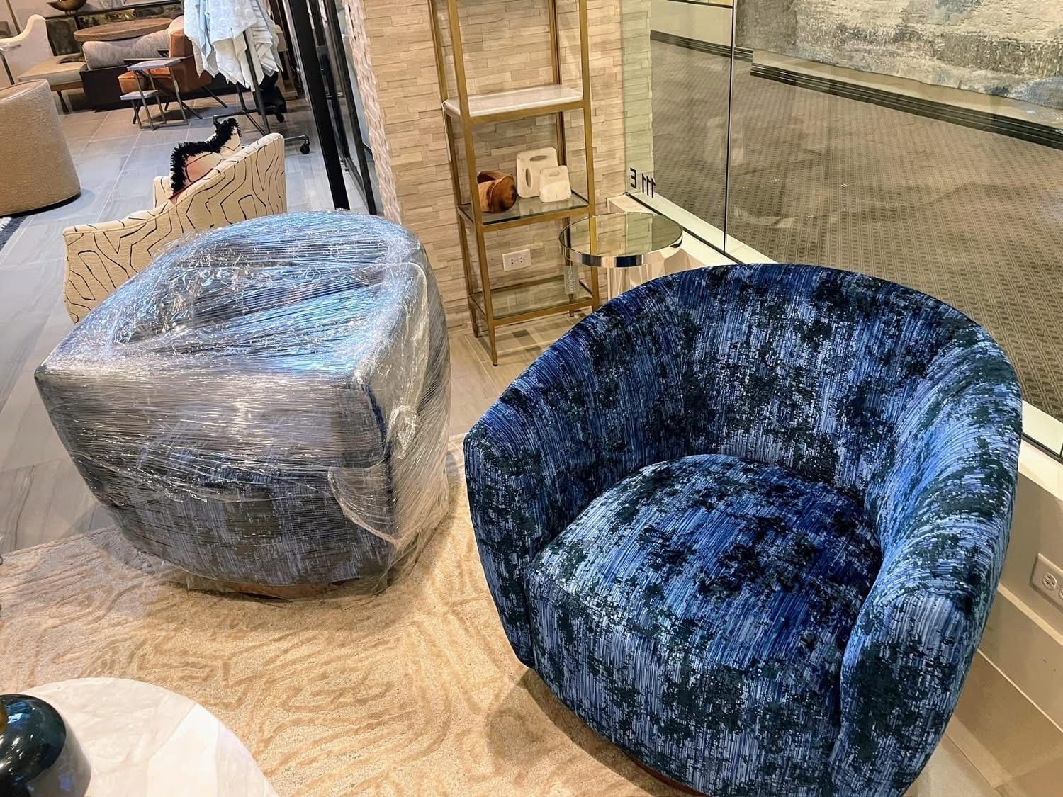 Two blue velvet armchairs, one wrapped in plastic, in a showroom.