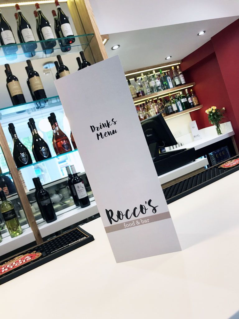 A bar with bottles of wine on shelves and a menu on the counter.