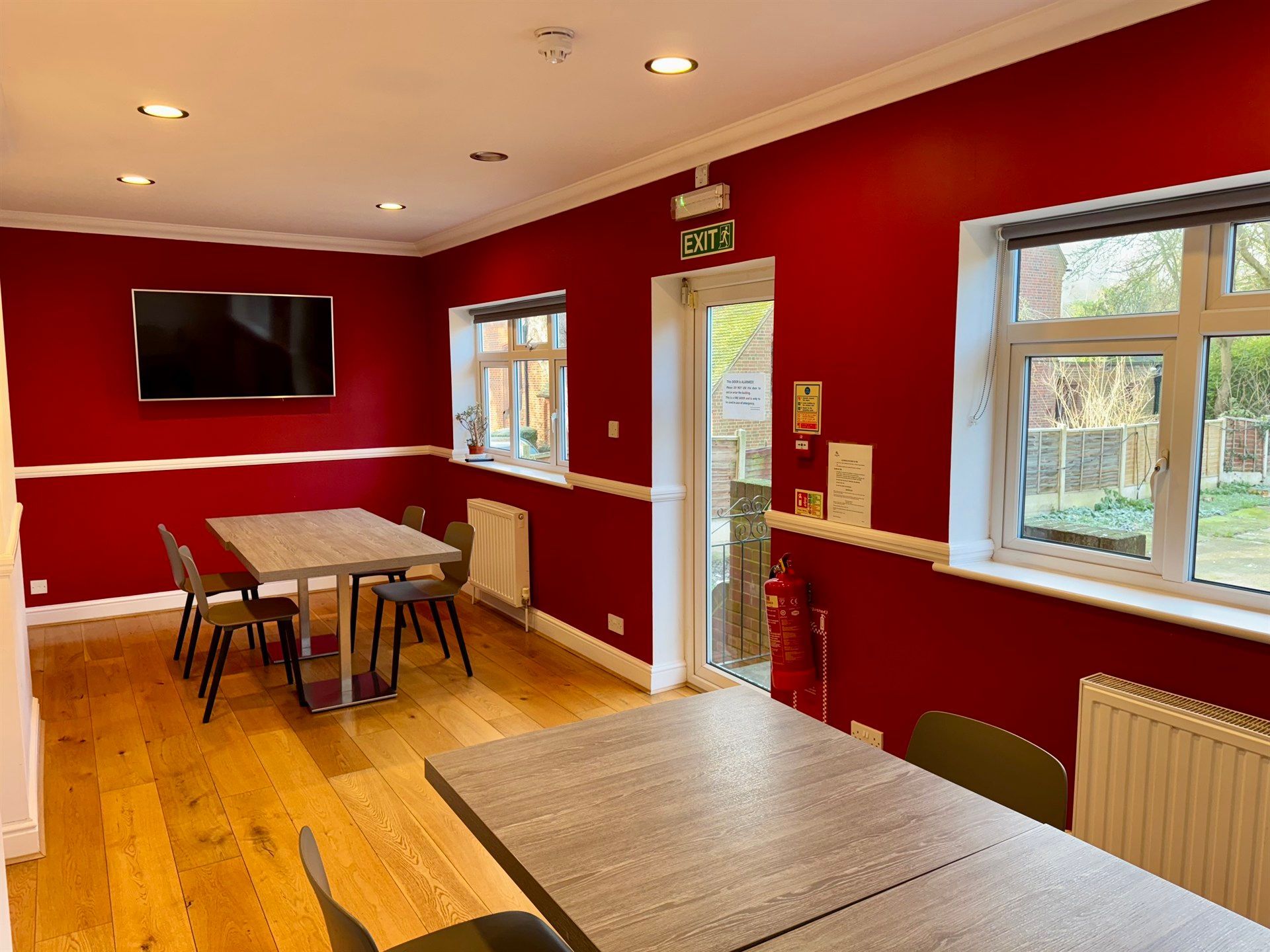 A room with red walls , tables and chairs and a flat screen tv.